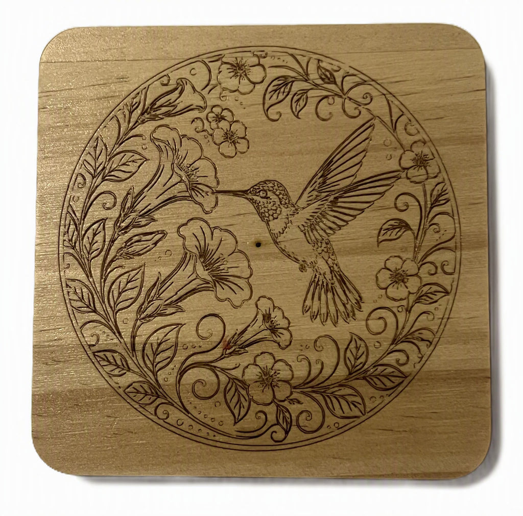 A square wooden coaster with rounded corners, featuring a circular laser-engraved design of a hummingbird and flowers.