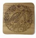 A square wooden coaster with rounded corners featuring a laser-engraved design of a sea turtle surrounded by marine plants, coral, bubbles, and a starfish.