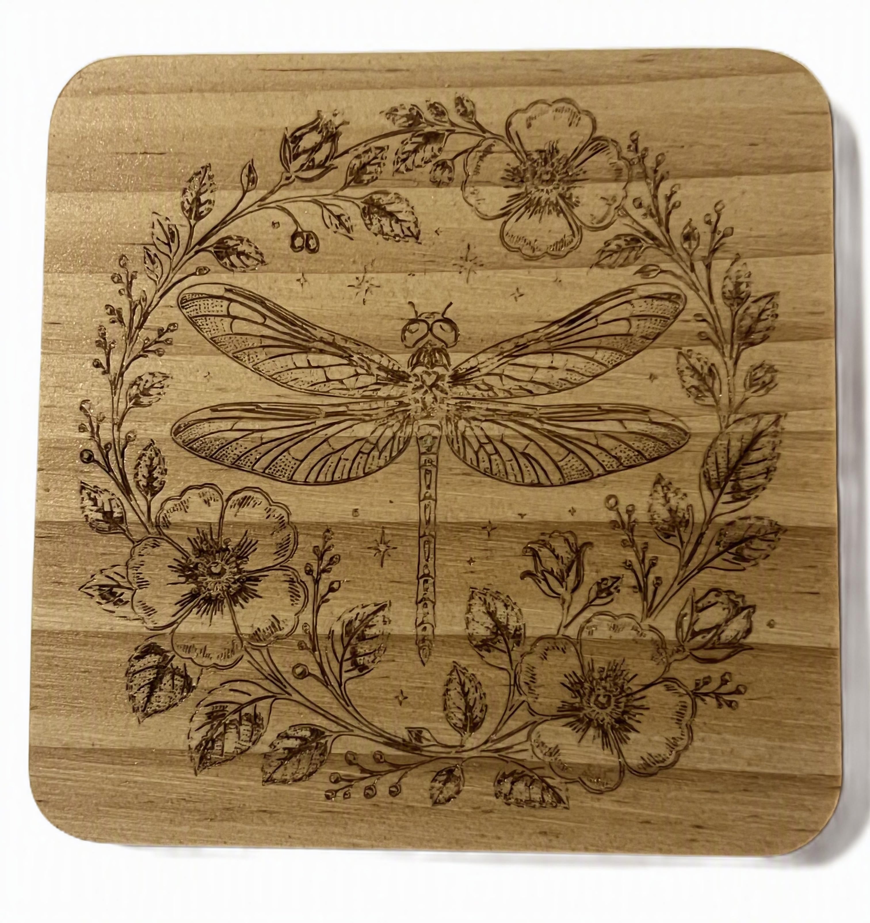 A square wooden coaster with rounded corners, featuring a laser-engraved design of a dragonfly surrounded by a floral wreath.