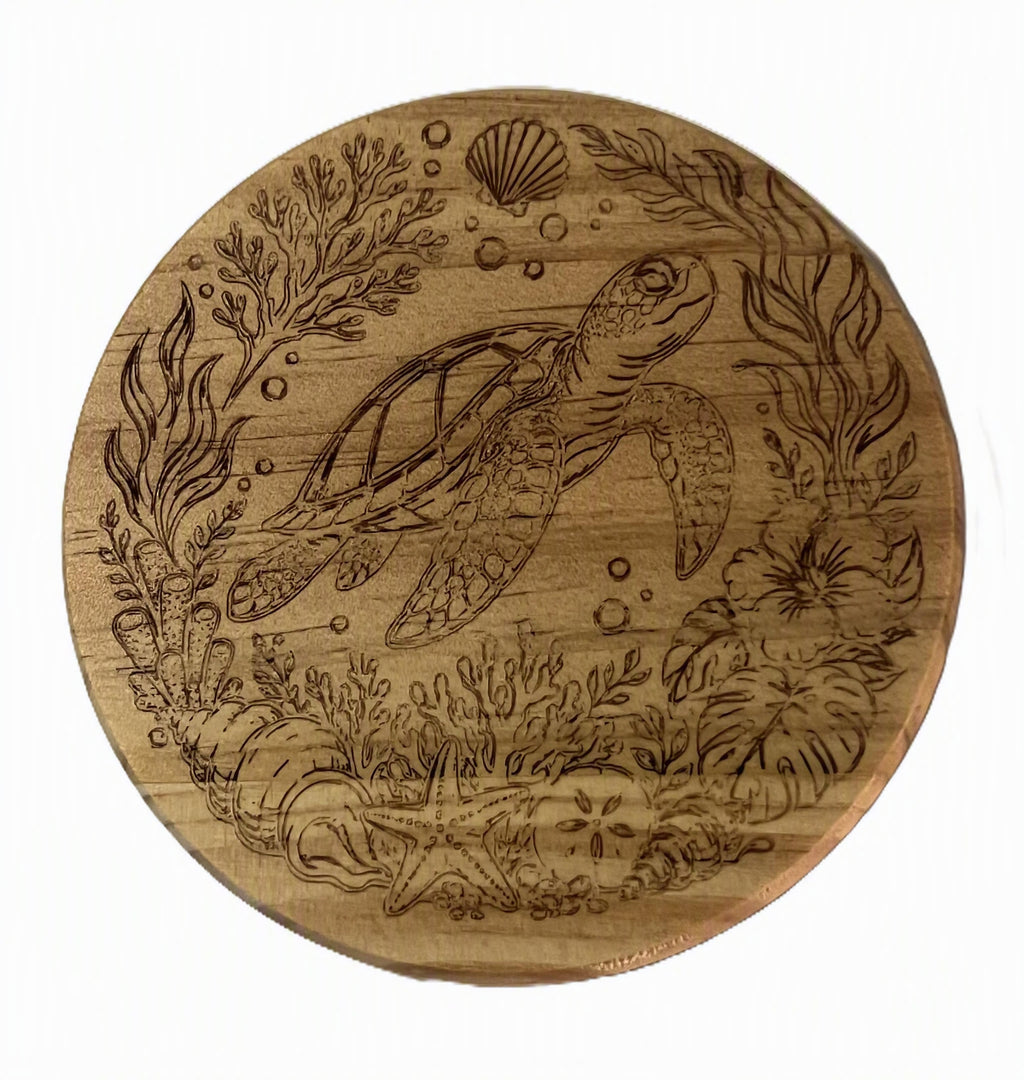 A round wooden coast plate engraved with an underwater scene featuring a sea turtle, seaweed, bubbles, and a shell.