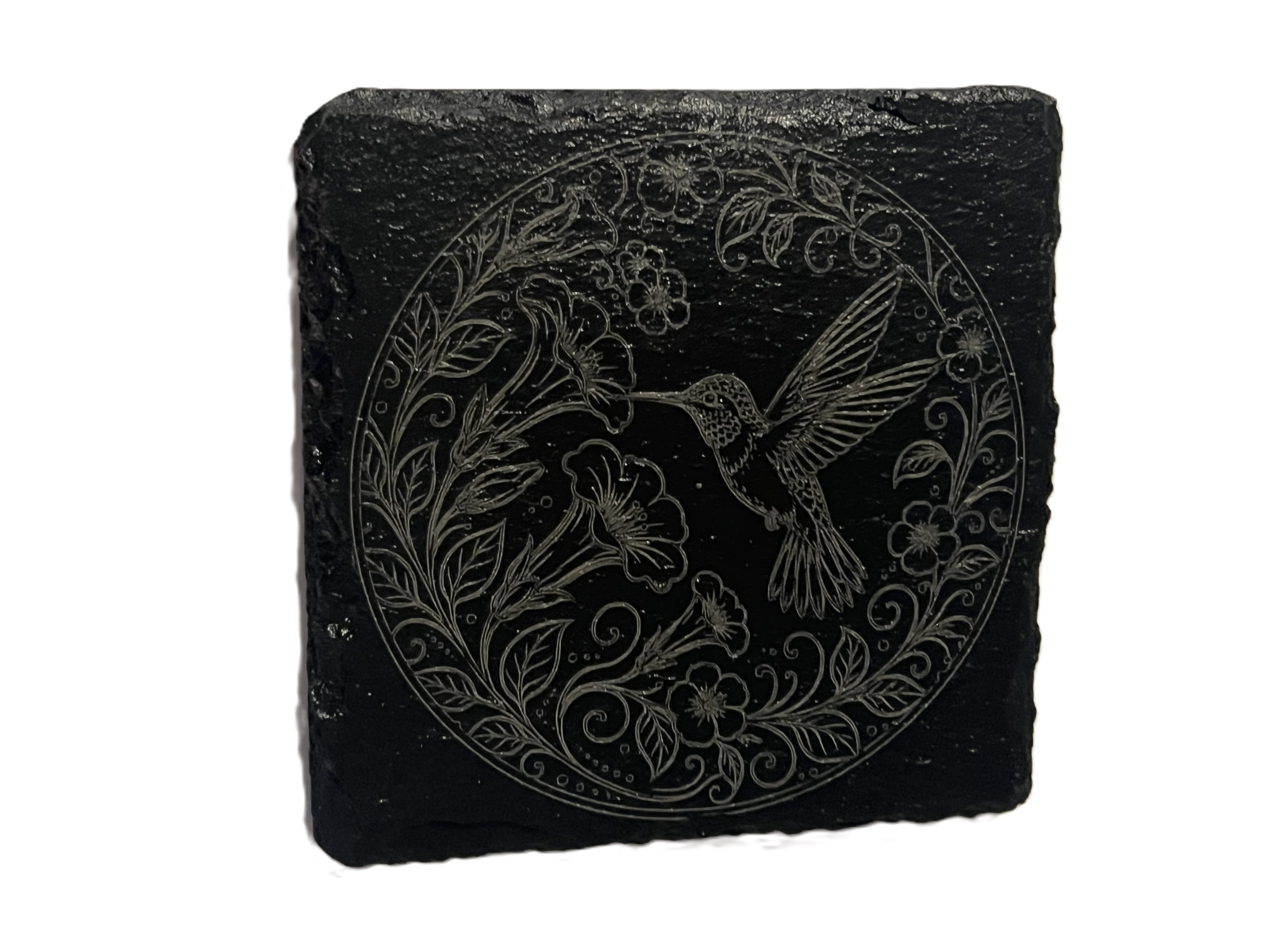 A square black slate coaster featuring an engraved circular design of a hummingbird and floral elements.