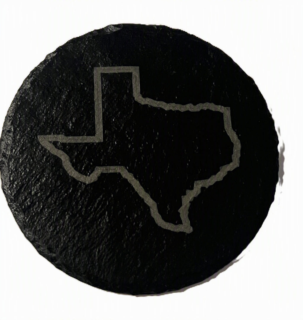 A round black slate coaster featuring a light gray outline of the state of Texas.