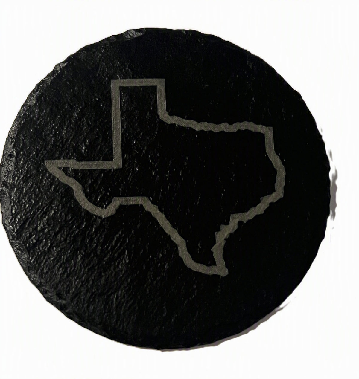 A round black slate coaster featuring a light gray outline of the state of Texas.